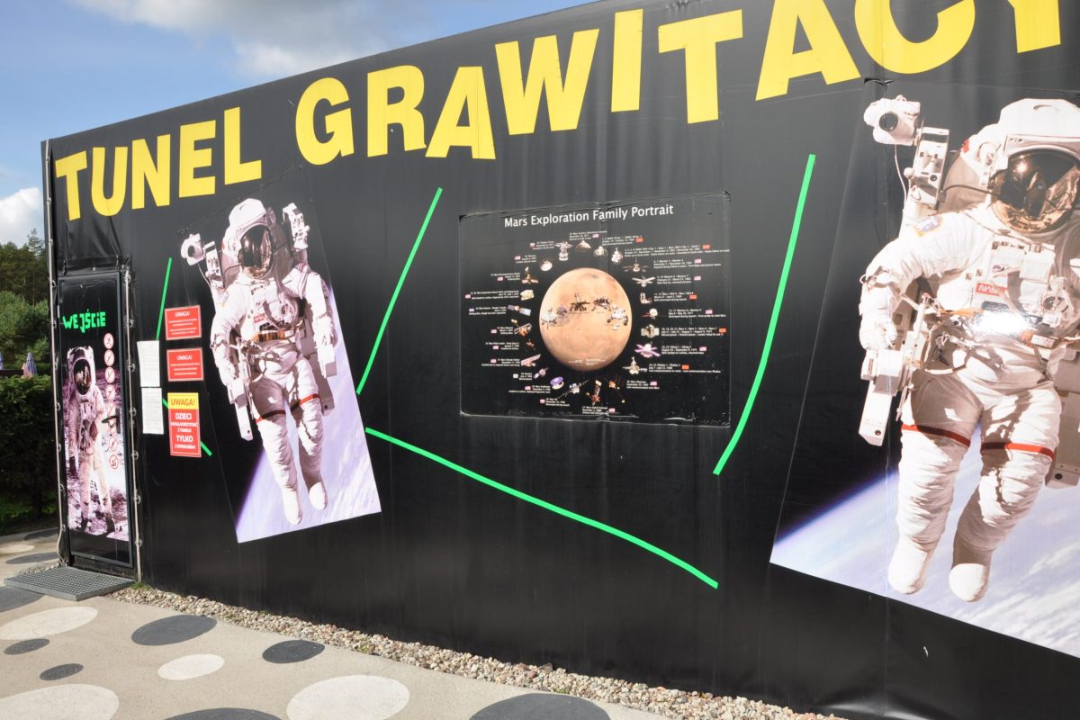 Tunel grawitacyjny w parku rozrywki blisko Białegostoku - Czarny budynek z napisem Tunel Grawitacji, zdjęciami astronautów i planszą o Mars Exploration Family Portrait.